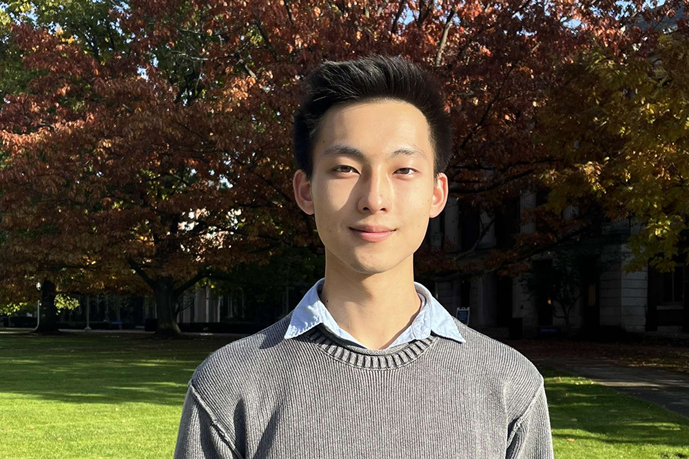Derek Chien posing for the camera with trees in the bacground.